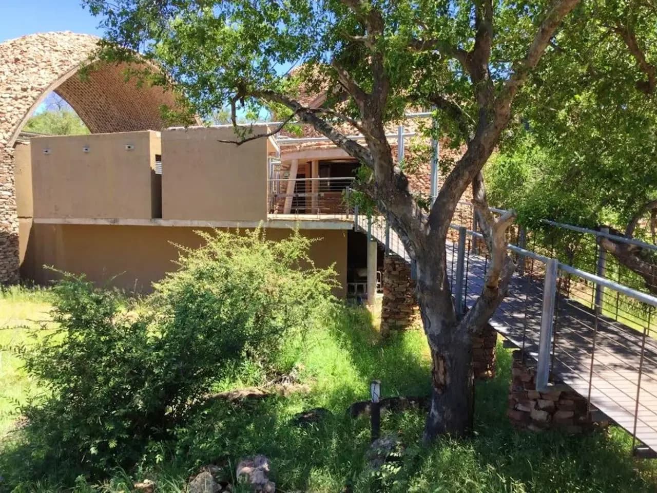 Ochre and white cottage with a terrace, trees and a metal-railed walkway, Leokwe Rest Camp