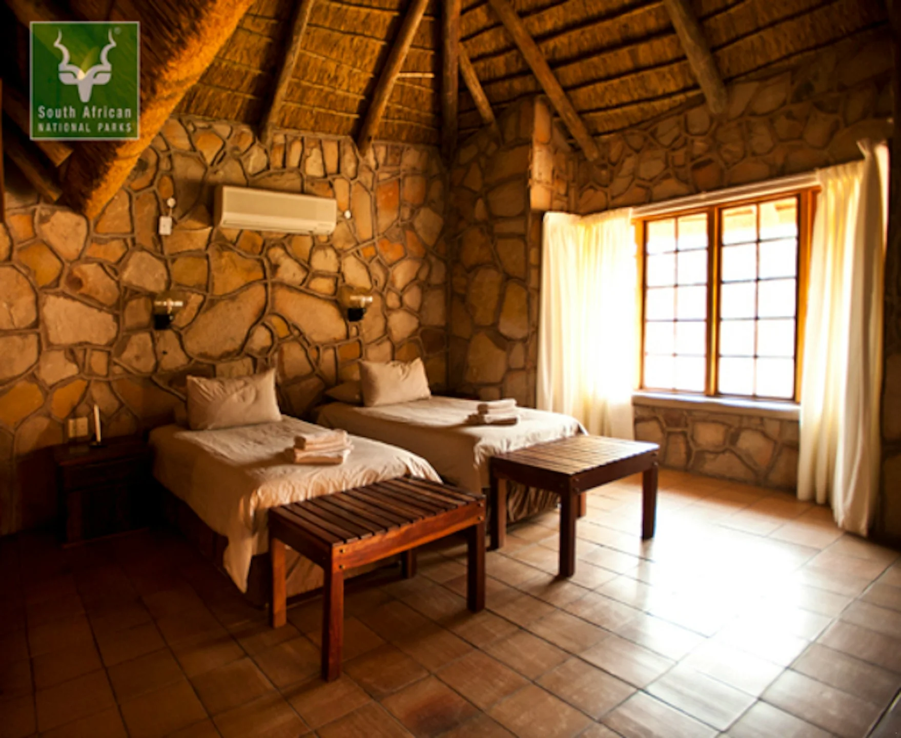 Twin beds in a stone-walled room beneath a thatched roof, Tshugulu Lodge
