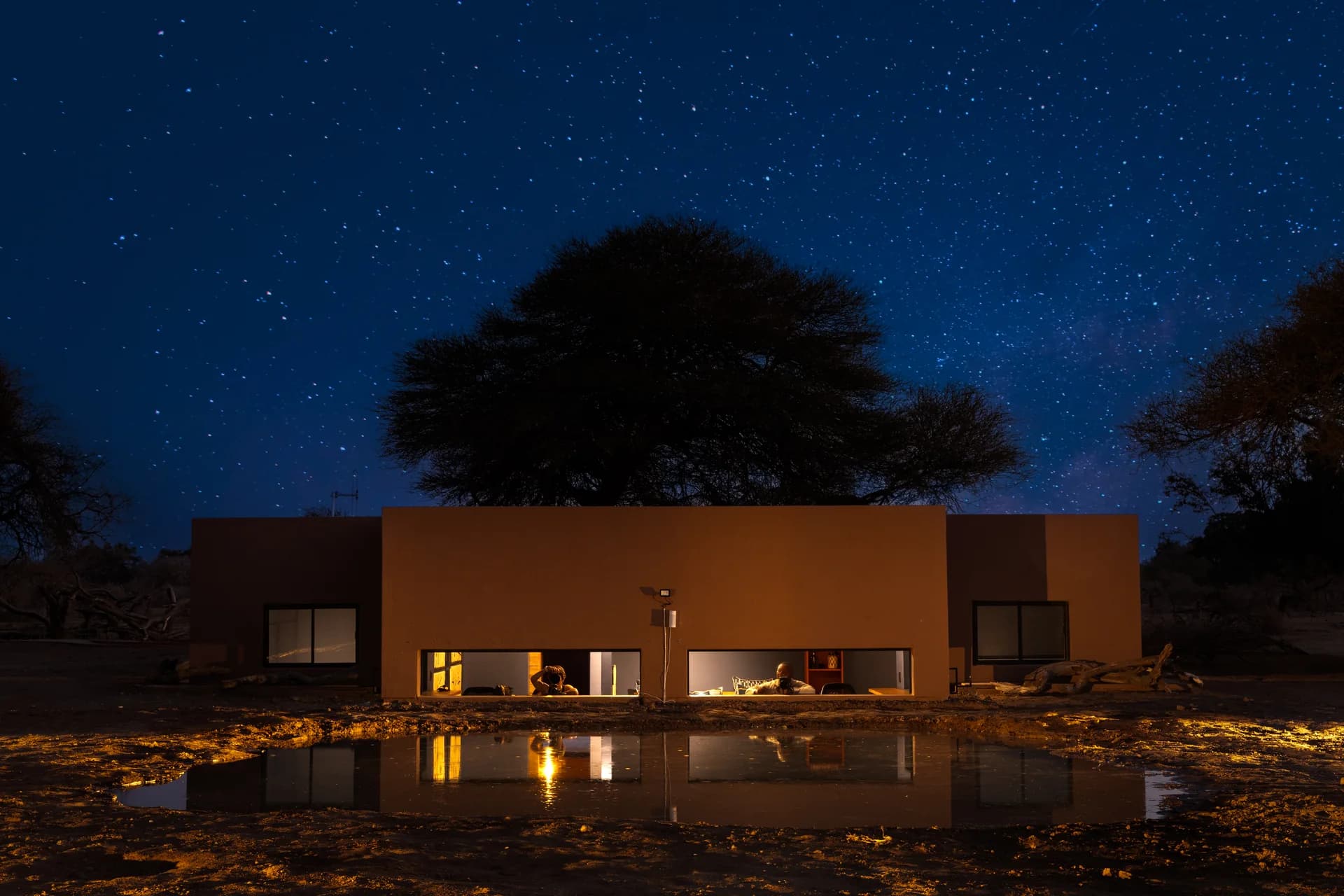 Illuminated hide building beside water under a starry sky, PhotoMashatu hides and photography