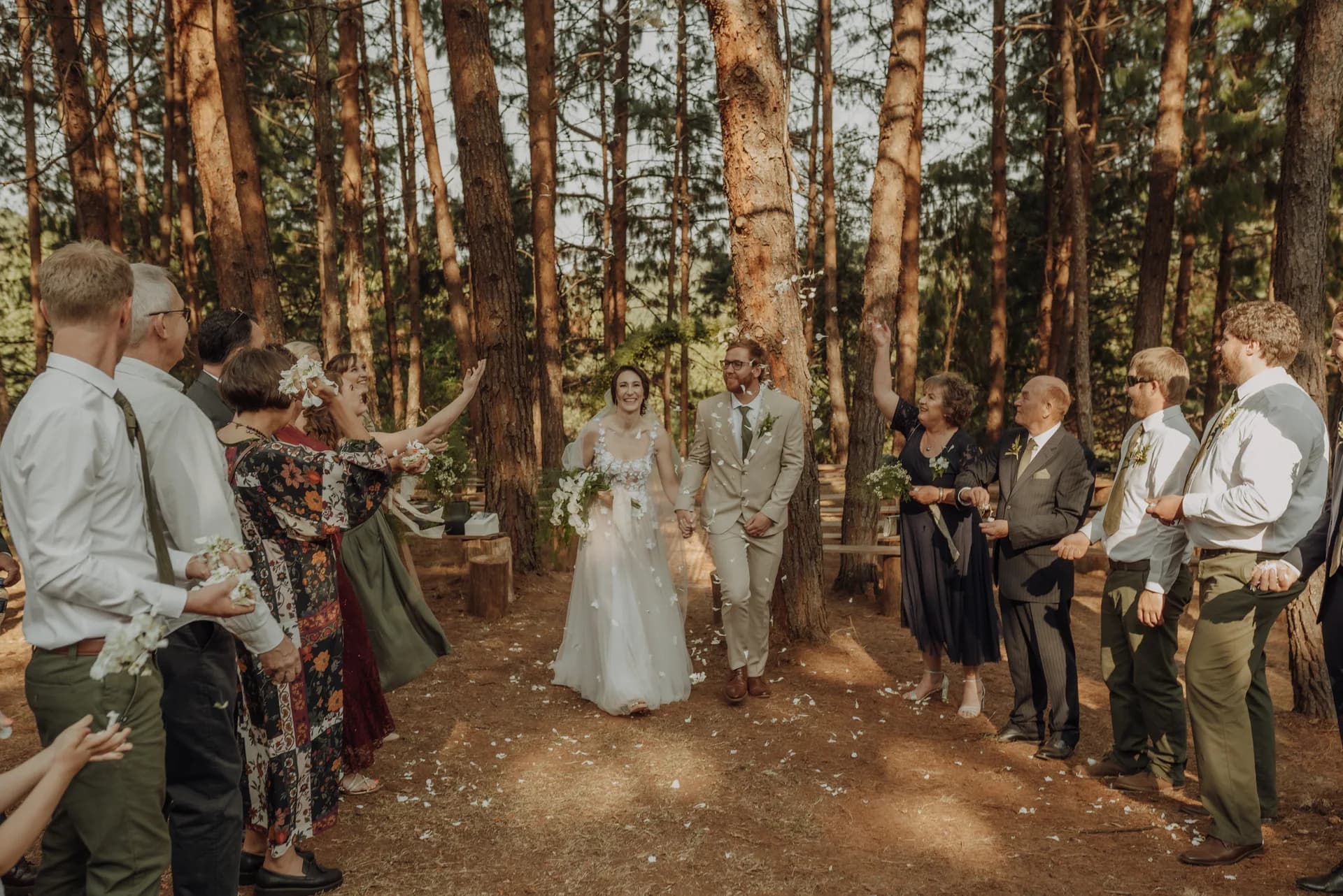 Wedding party gathered beneath tall trees in a woodland ceremony setting, Mina's Farm Venue