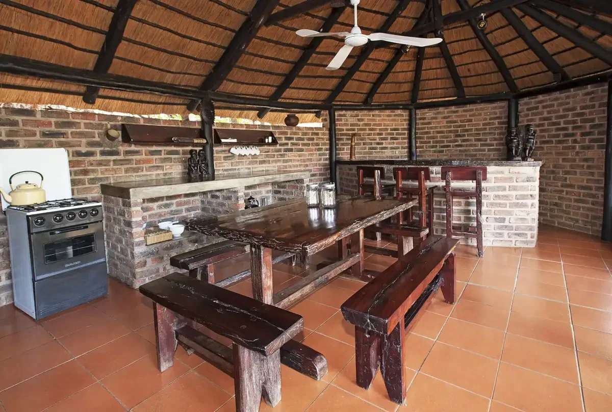 Thatched brick kitchen and dining room with wooden benches and a ceiling fan, Limpopo River Lodge Botswana